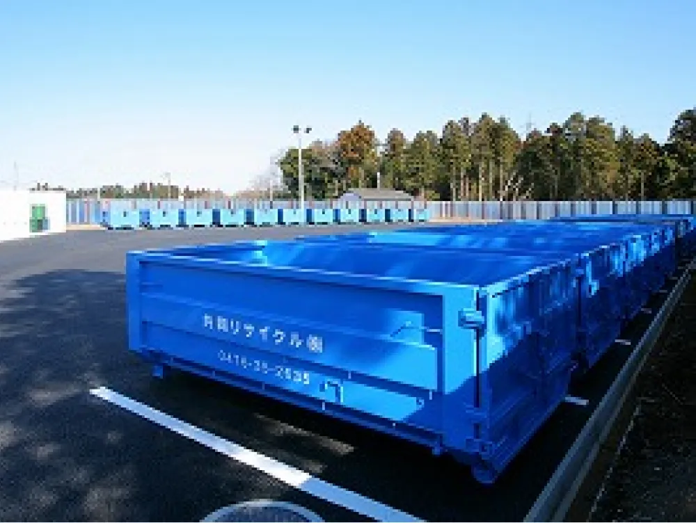 共同リサイクル株式会社の青いコンテナが駐車場に複数台整列して並んでいる